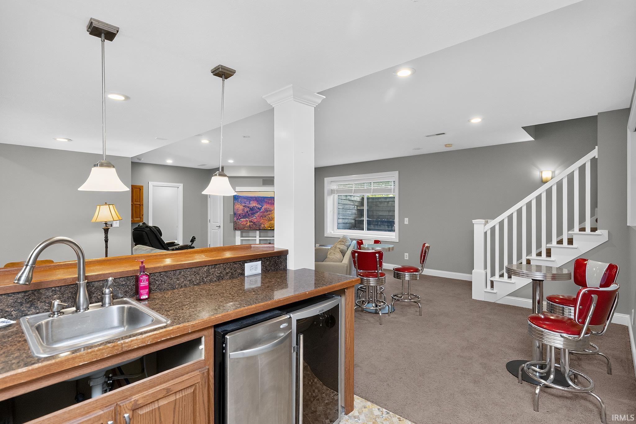 Integrated wet bar featuring a stainless steel sink, wood-finish cabinetry, and a beverage refrigerator