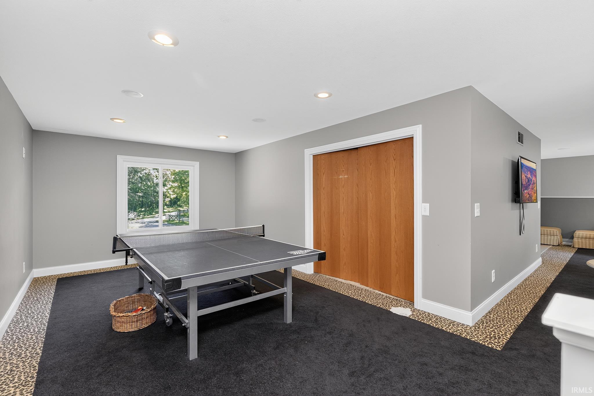 Recreation room featuring recessed lighting, a window with exterior views, light gray walls, white trim, and a built-in closet with wood-finish bi-fold doors
