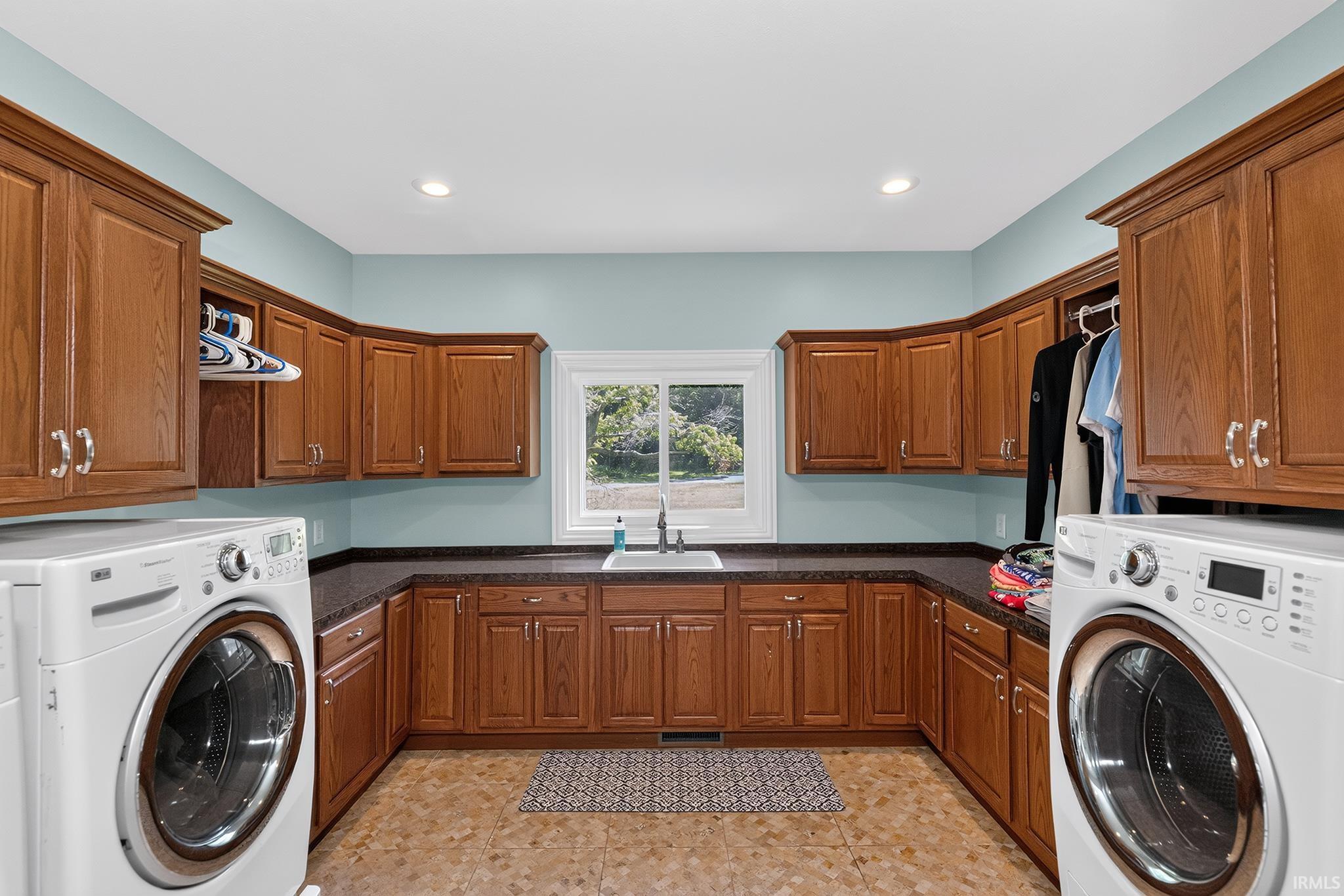 Spacious laundry room featuring extensive wood cabinetry, dark countertops, a built-in sink, window with natural light, and recessed lighting