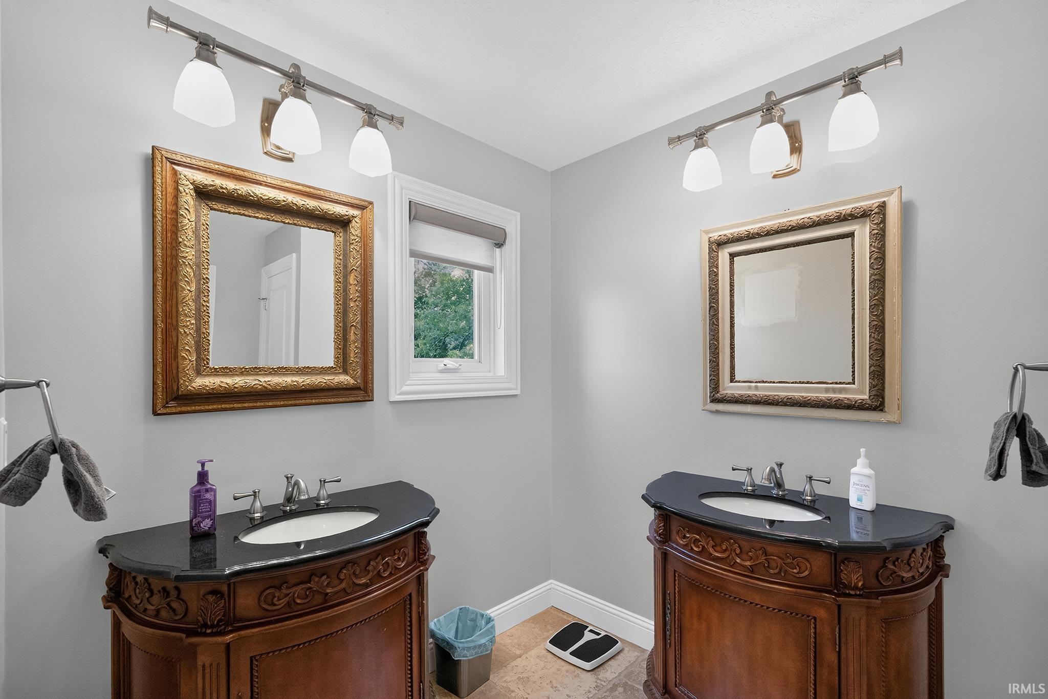 Dual vanity setup featuring ornate wood cabinetry with dark countertops, under-mount sinks, and framed mirrors