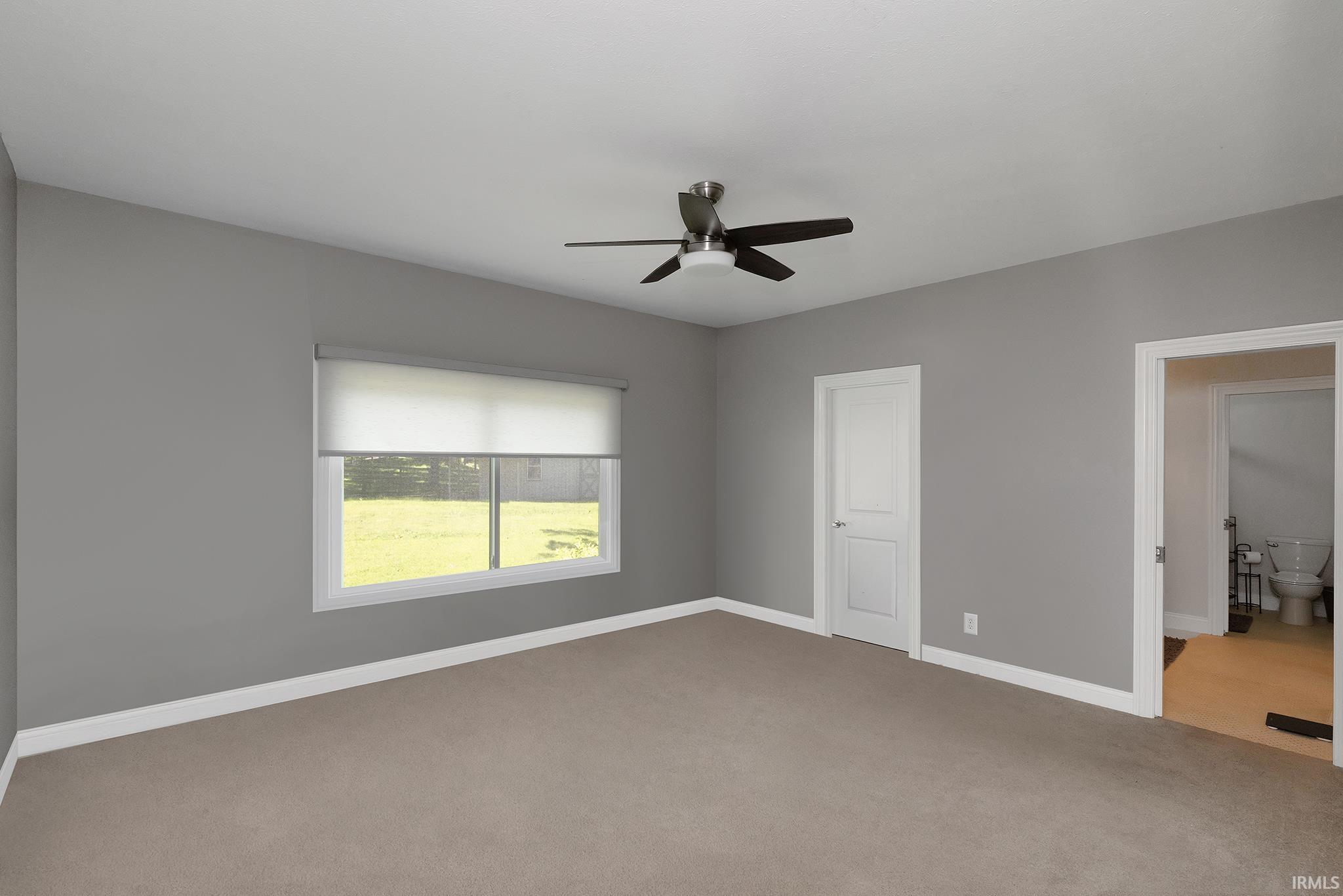 Spacious room featuring neutral carpeting, a large window with roller shades, and a contemporary ceiling fan with integrated lighting