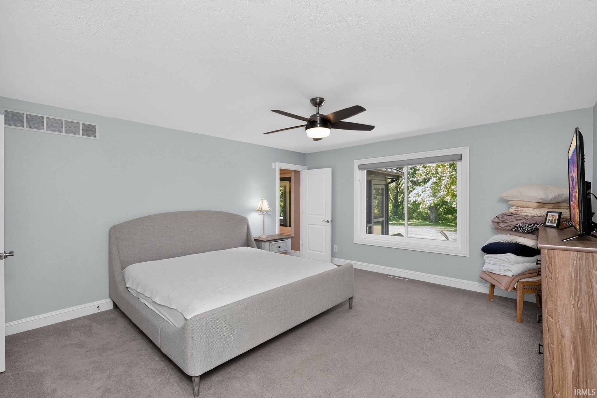Spacious room featuring light blue walls, gray carpeting, a large window with white trim, and a ceiling fan with integrated lighting