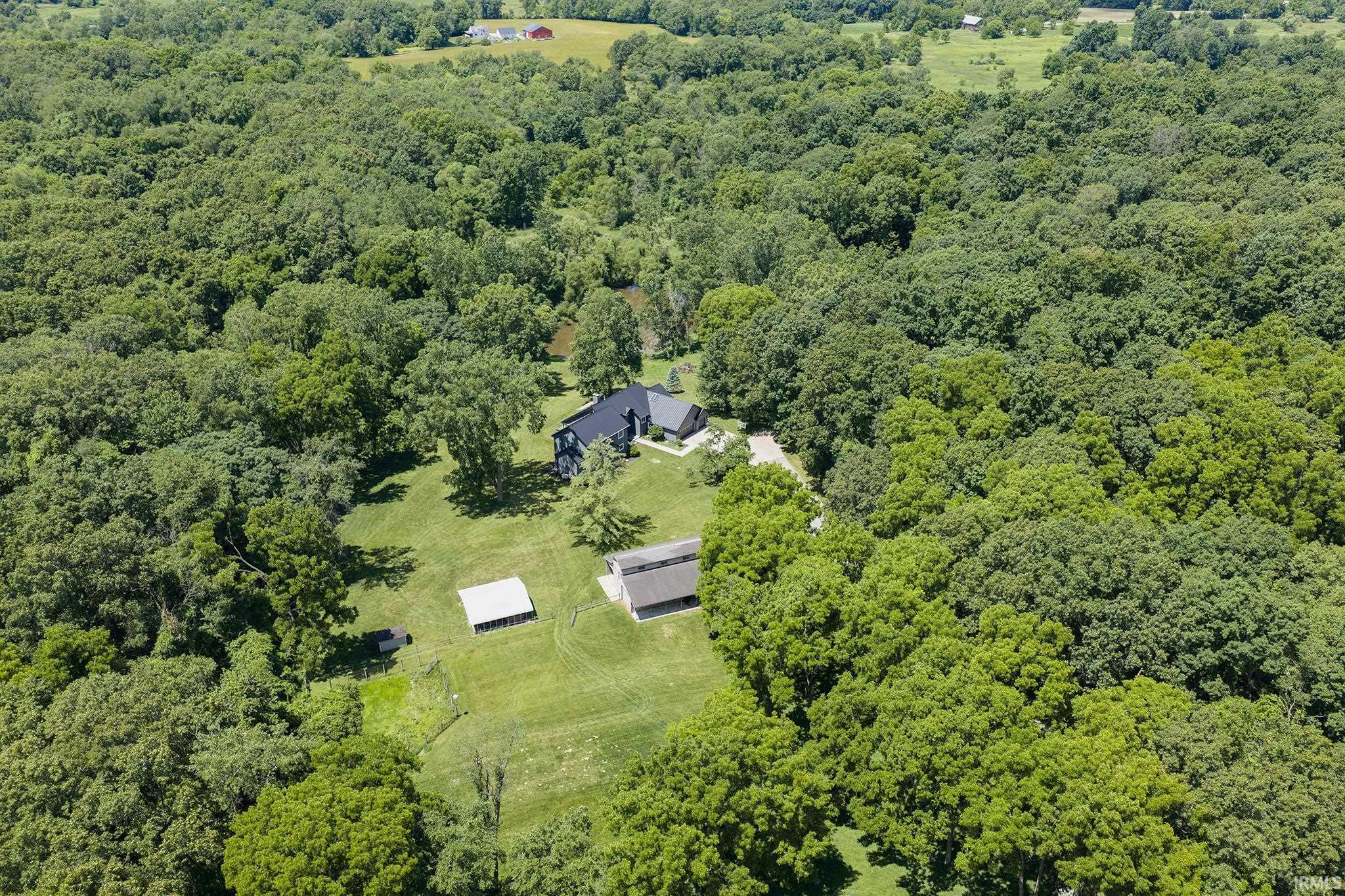 Expansive property featuring a contemporary dark-toned residence, surrounded by mature trees