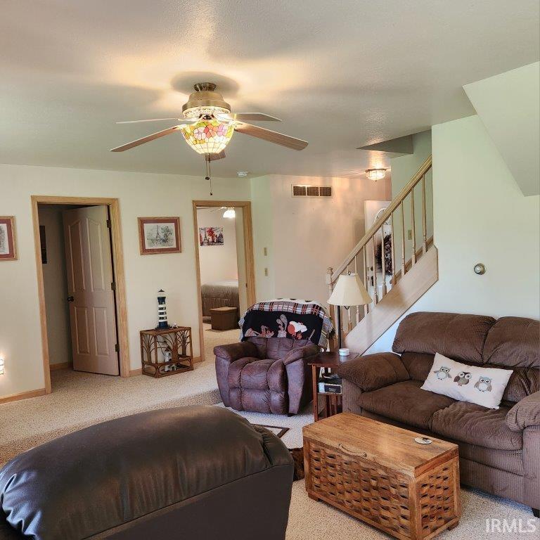 Carpeted living area featuring a ceiling fan with an ornate light fixture, light-colored walls, and wood-trimmed doorways