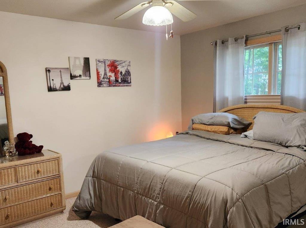 Carpeted room featuring a ceiling fan with integrated lighting, a window with horizontal blinds, and a built-in wall mirror