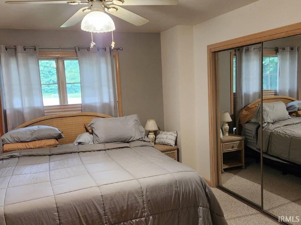 Bedroom featuring a ceiling fan with integrated lighting, a window with horizontal blinds and curtain rods, and a mirrored closet with wood-finish trim