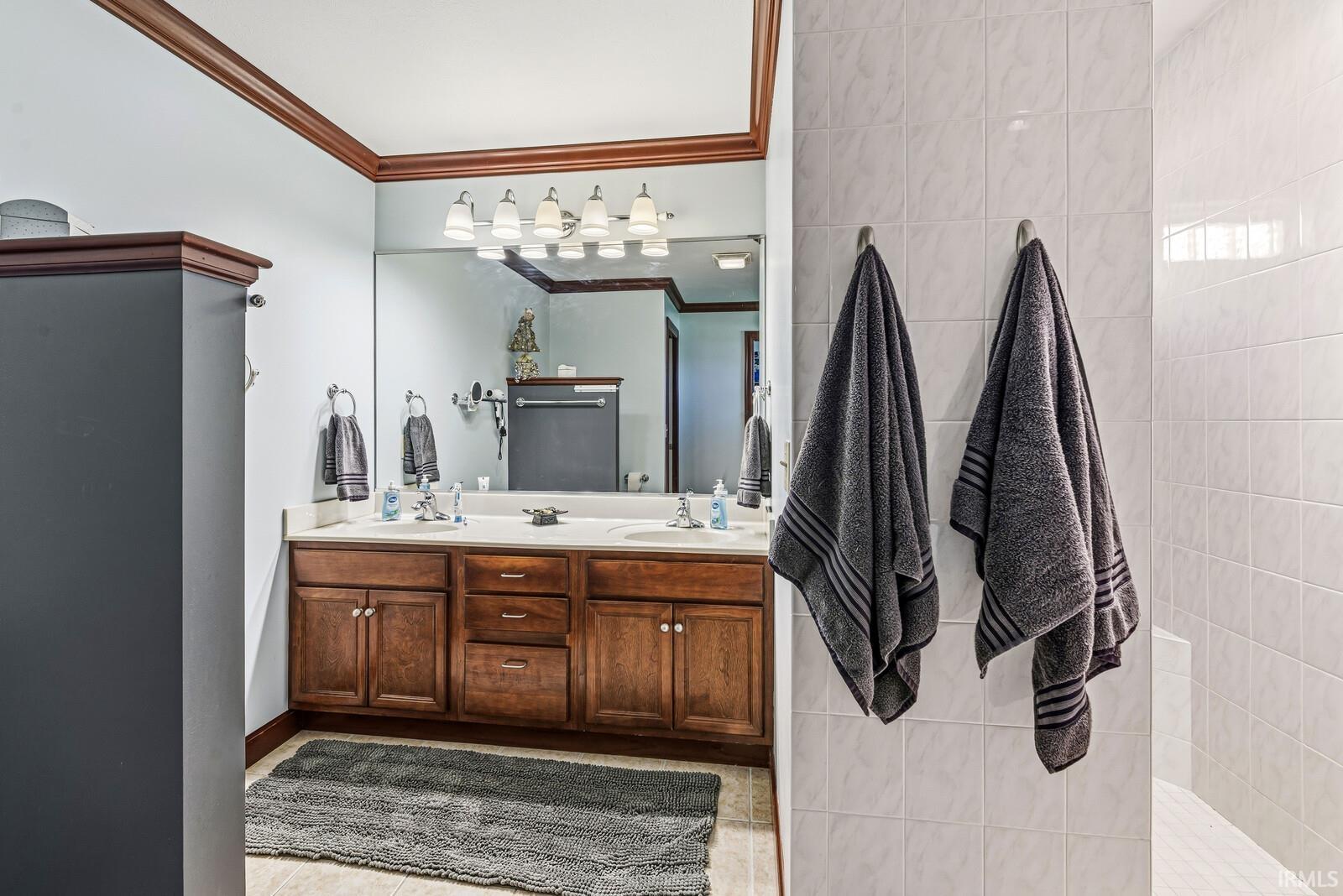 Bathroom featuring a double vanity with wood cabinetry, a large mirror, a chrome multi-bulb light fixture, and tile flooring