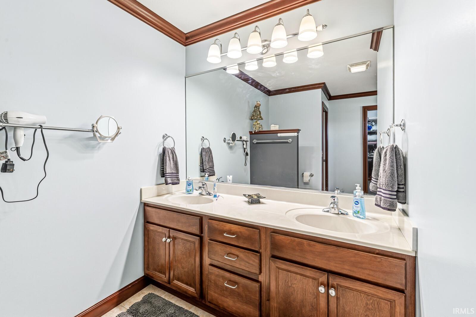 Dual vanity with wood-finish cabinetry and integrated sinks, featuring a large wall-mounted mirror and overhead lighting fixture