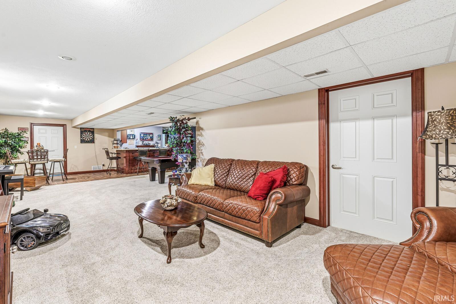 Spacious finished lower level featuring light-toned carpeting, a built-in wet bar with seating, and a drop ceiling with recessed lighting