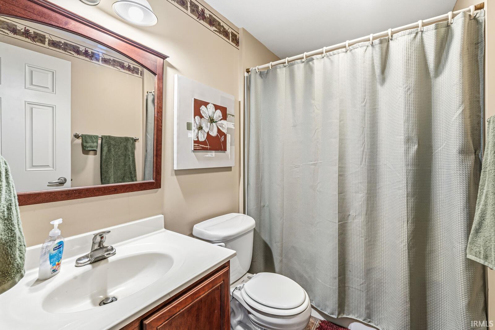 Bathroom featuring a vanity with a white countertop and integrated sink, a dark wood-finish cabinet, a framed mirror, a toilet, and a shower area