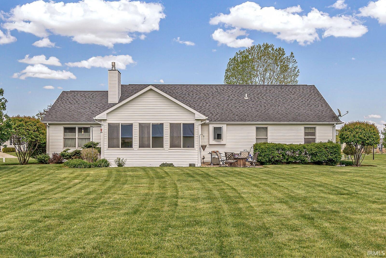 Rear exterior featuring an expansive lawn, white horizontal siding, a gabled roofline, and established landscaping
