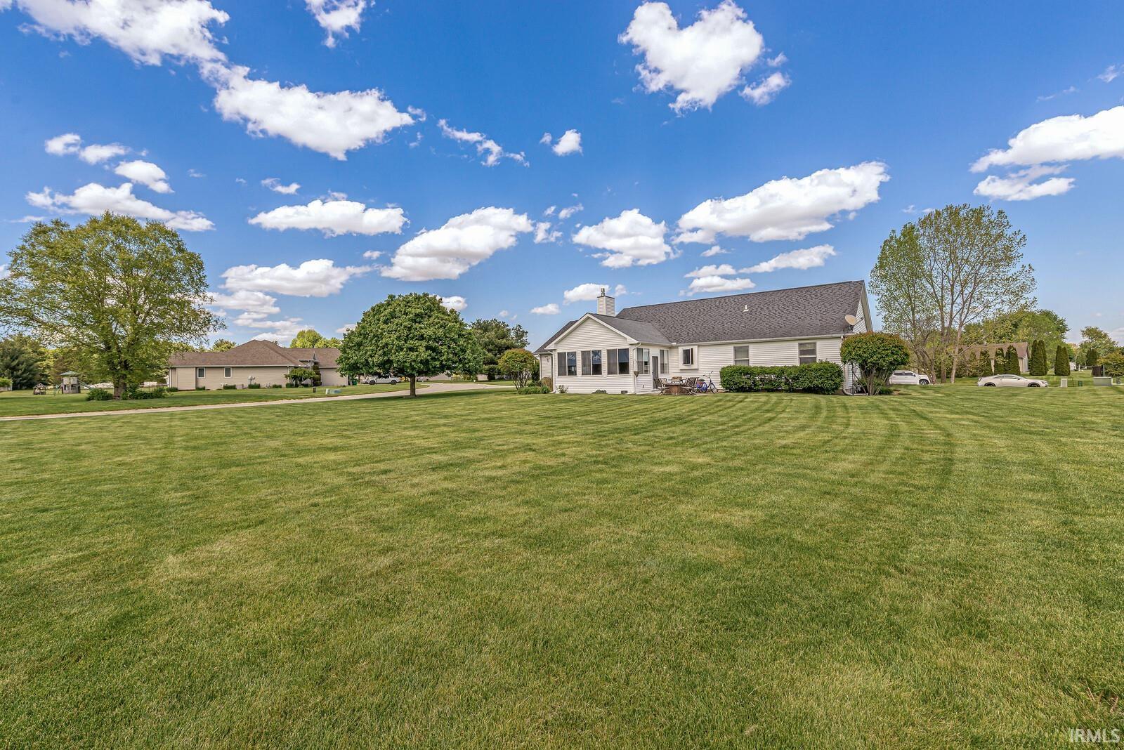 Expansive green space featuring a white stucco exterior, multiple large mature trees, a dark shingle roof, and an enclosed patio area