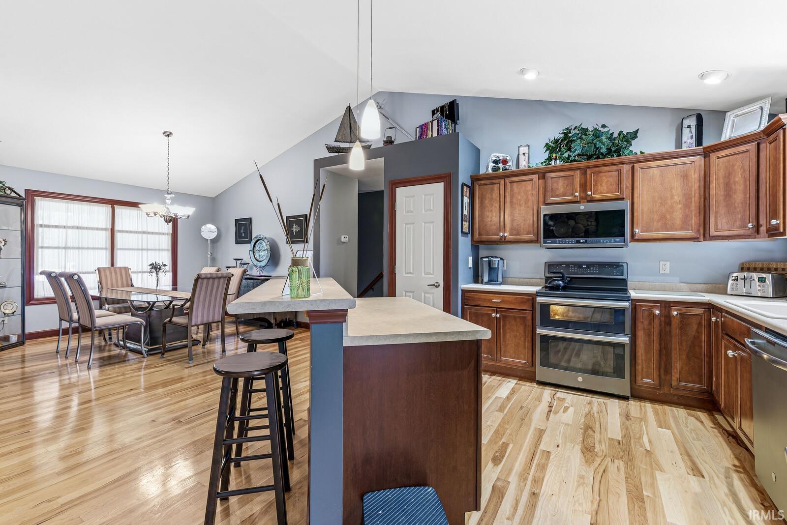 Open-concept living area featuring a kitchen island with seating, wood-finish flooring, vaulted ceilings, a dining area with ample natural light, and classic wood cabinetry