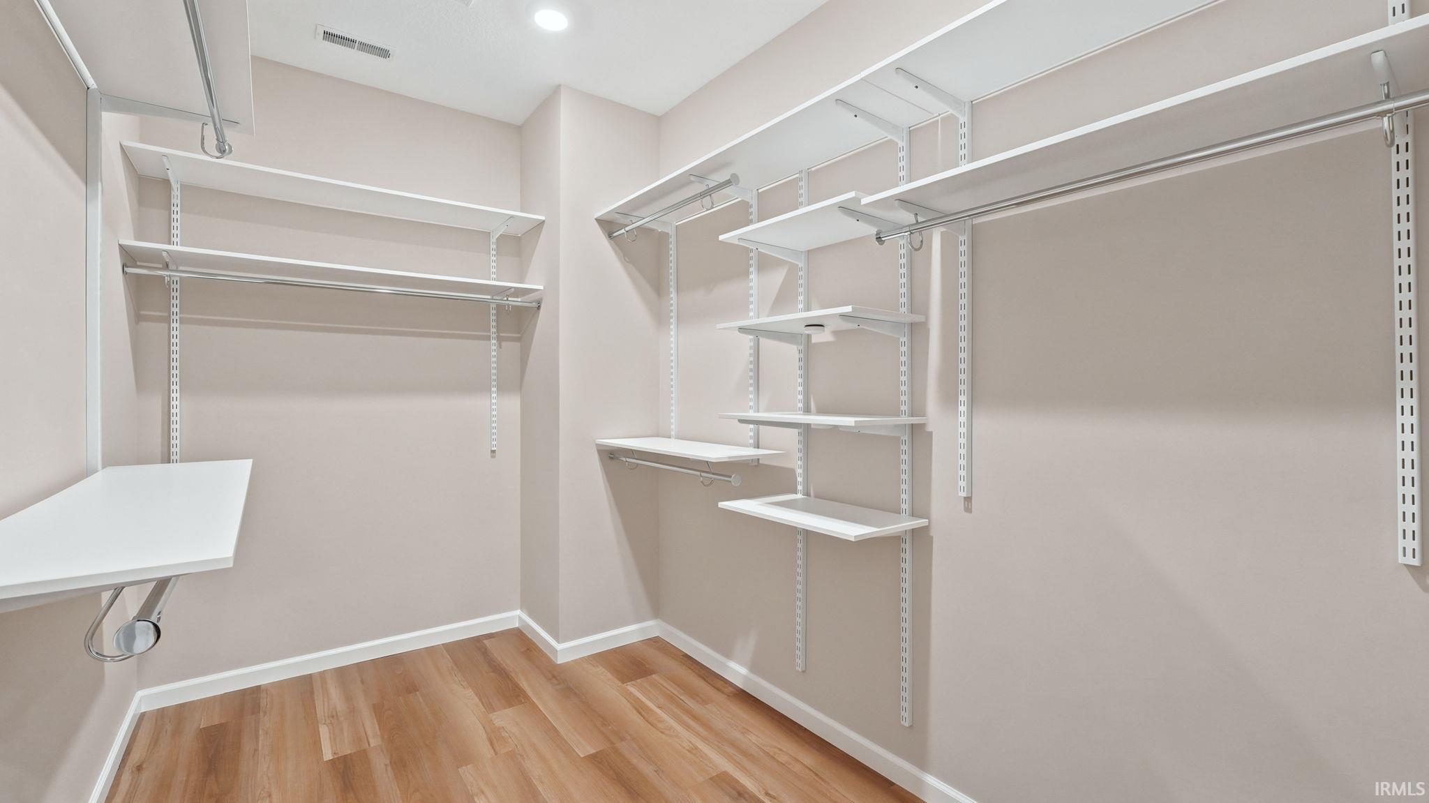 Walk-in closet featuring wood-finish flooring, recessed lighting, and white adjustable shelving systems