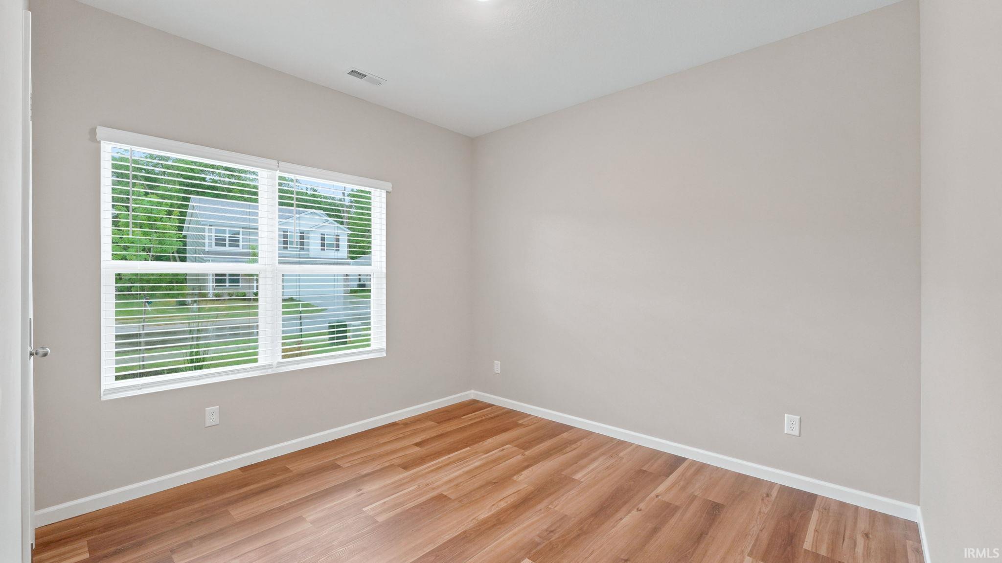 Light-filled room featuring wood-finish flooring, neutral wall paint, white trim, a large window with blinds, and a ceiling light fixture