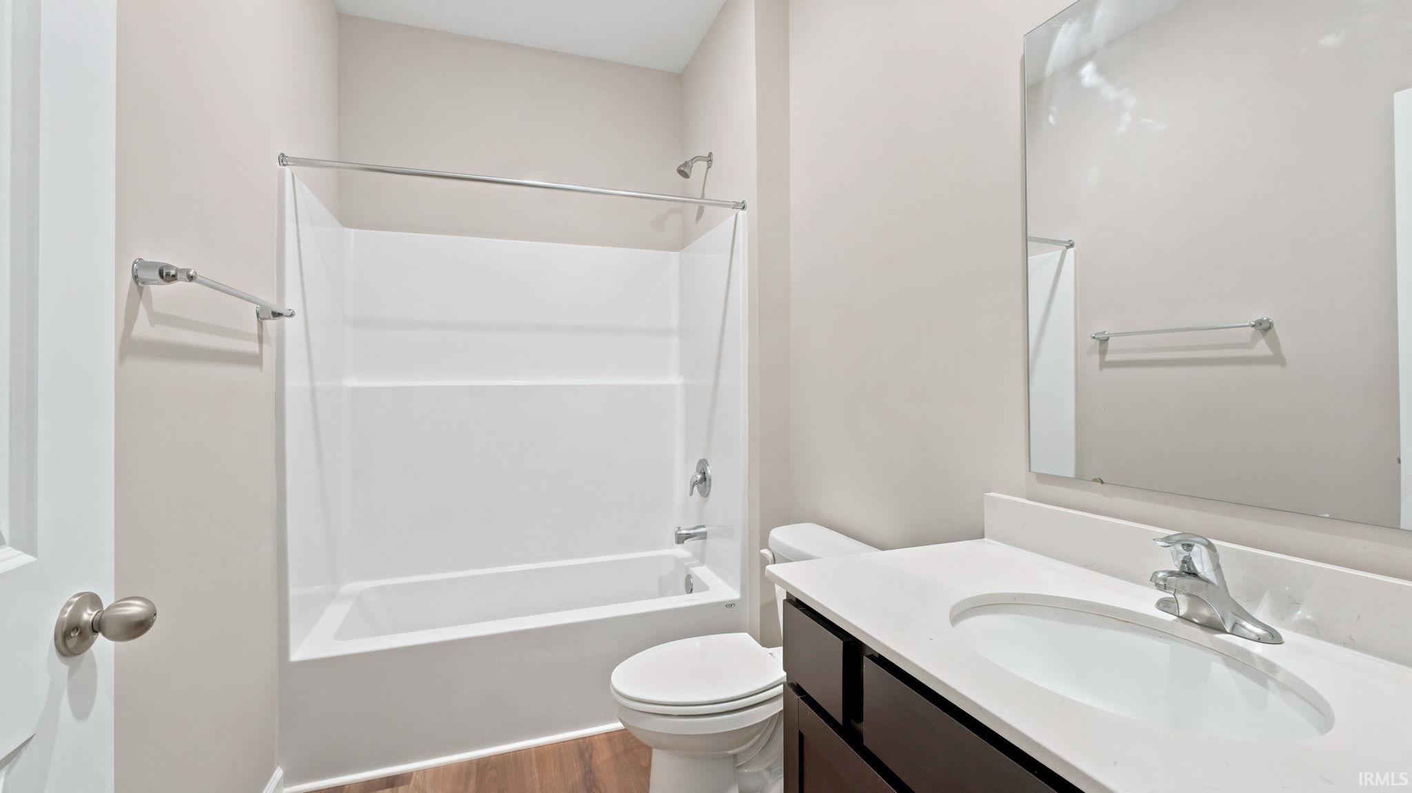 Bathroom featuring a white tub/shower combination, dark wood-finish vanity with a white countertop, and a large wall-mounted mirror