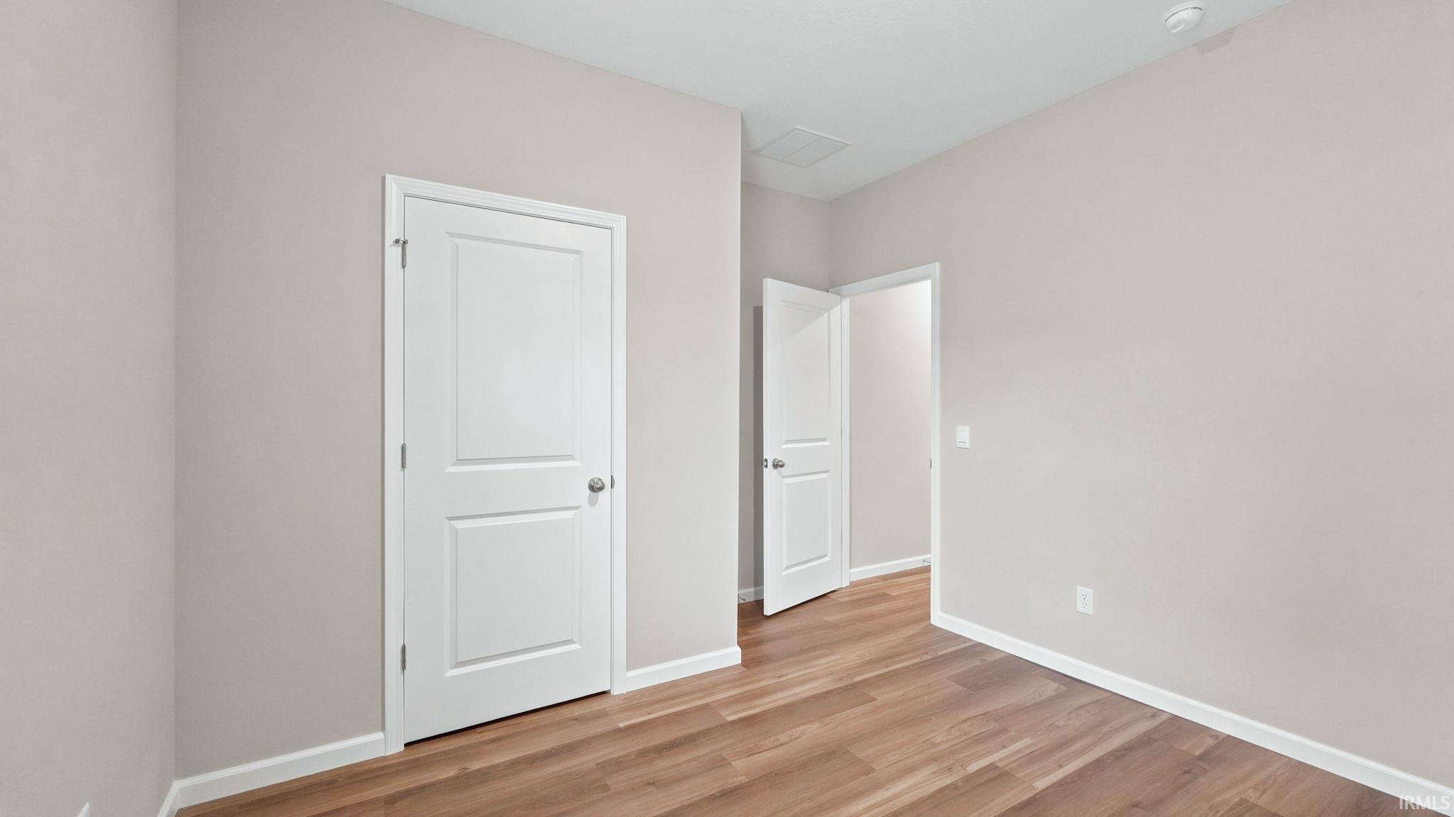 Room with wood-finish flooring, light neutral wall paint, white baseboards, and two-panel interior doors