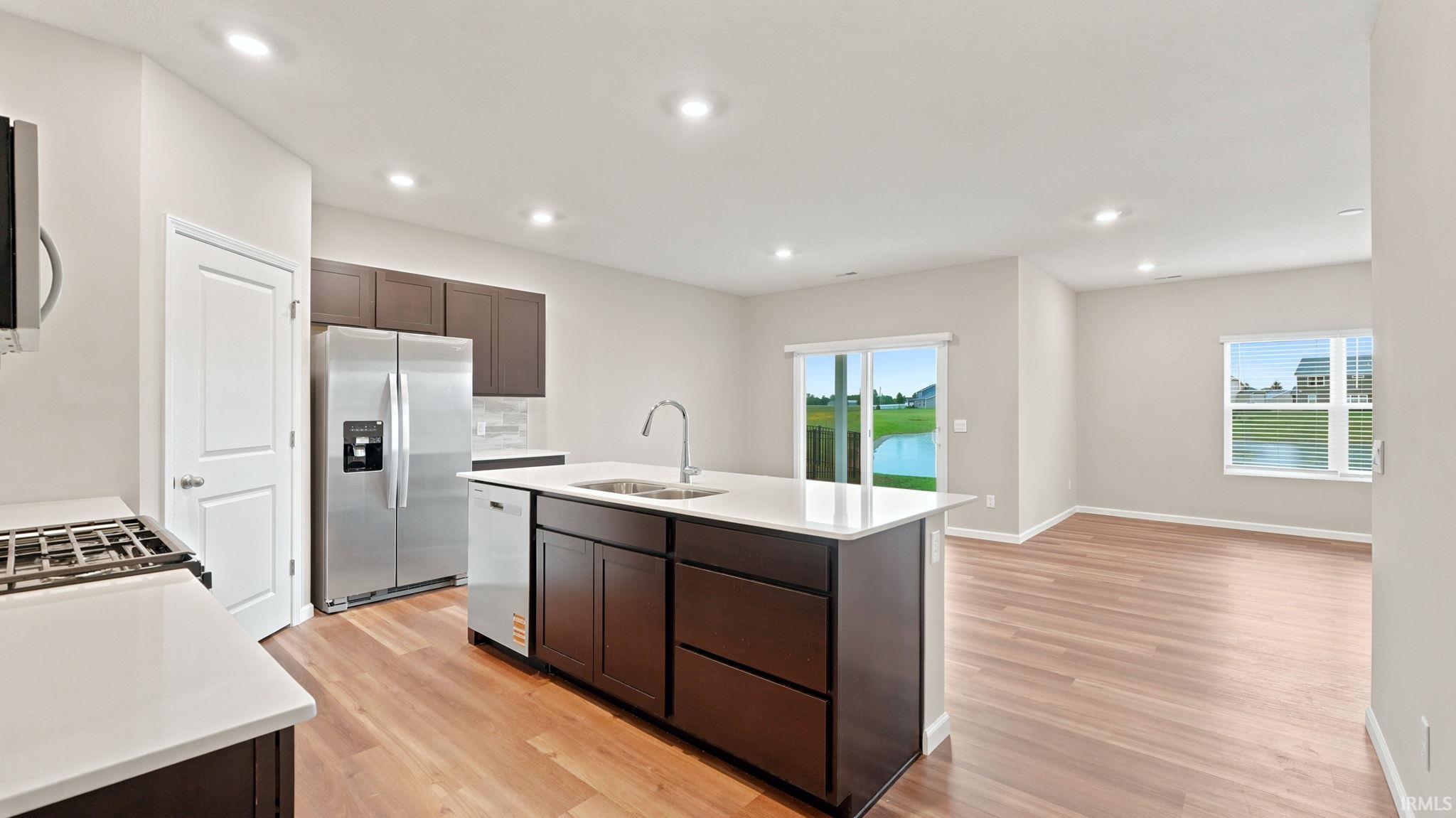 Open-concept kitchen featuring an island with integrated sink, stainless steel appliances, wood-finish flooring, and recessed lighting