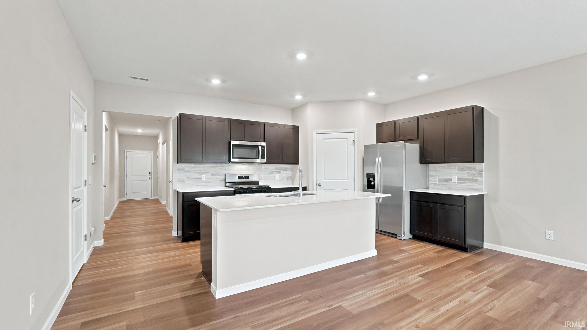 Contemporary kitchen featuring an island, dark wood cabinetry, stainless steel appliances, light countertops, and wood-finish flooring