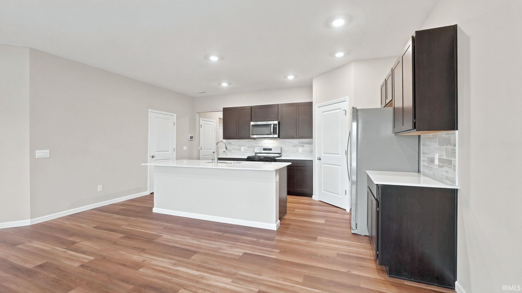 Open-concept kitchen with wood-finish flooring, recessed lighting, a central island, dark cabinetry, and light-colored countertops