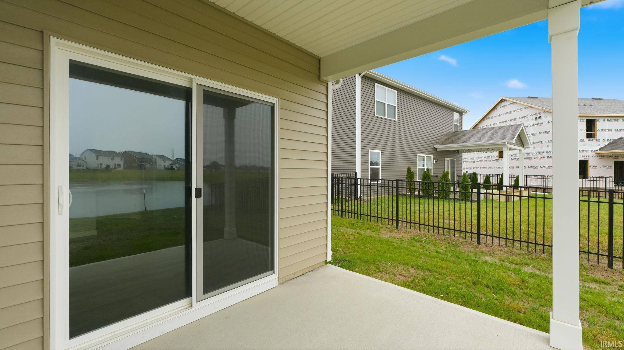 Covered concrete patio with sliding glass door entry, vinyl siding exterior, and a black wrought iron fence