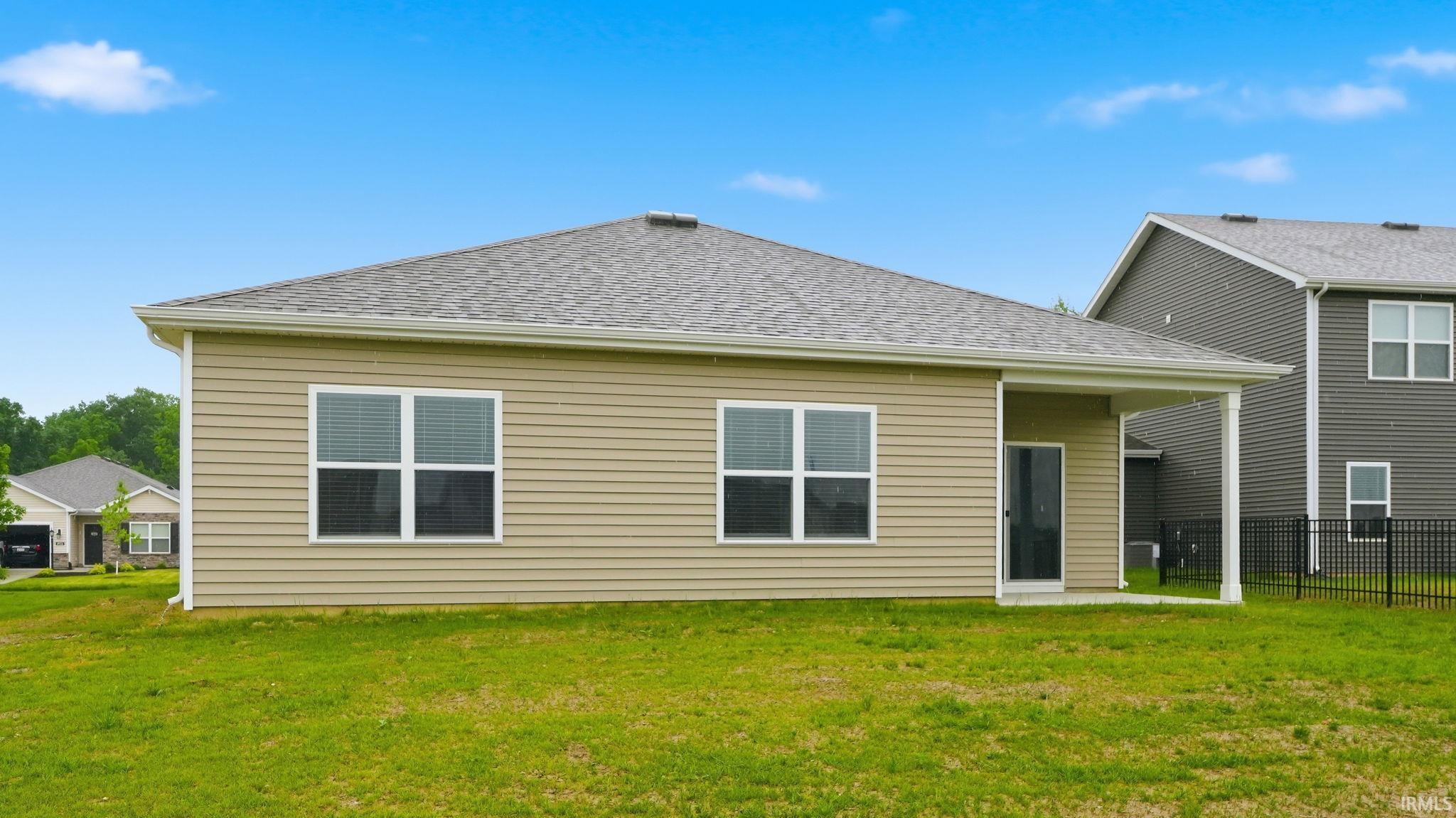 Expansive rear yard featuring a covered patio, tan horizontal siding, and a gabled shingle roof