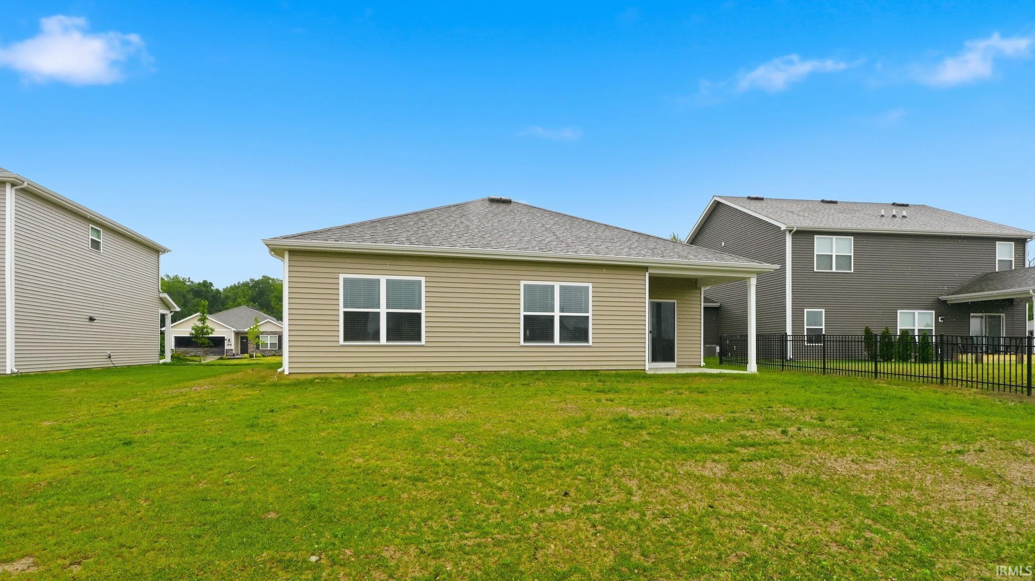 Expansive rear yard featuring a covered patio, tan horizontal siding, multiple windows, and a black fenced perimeter