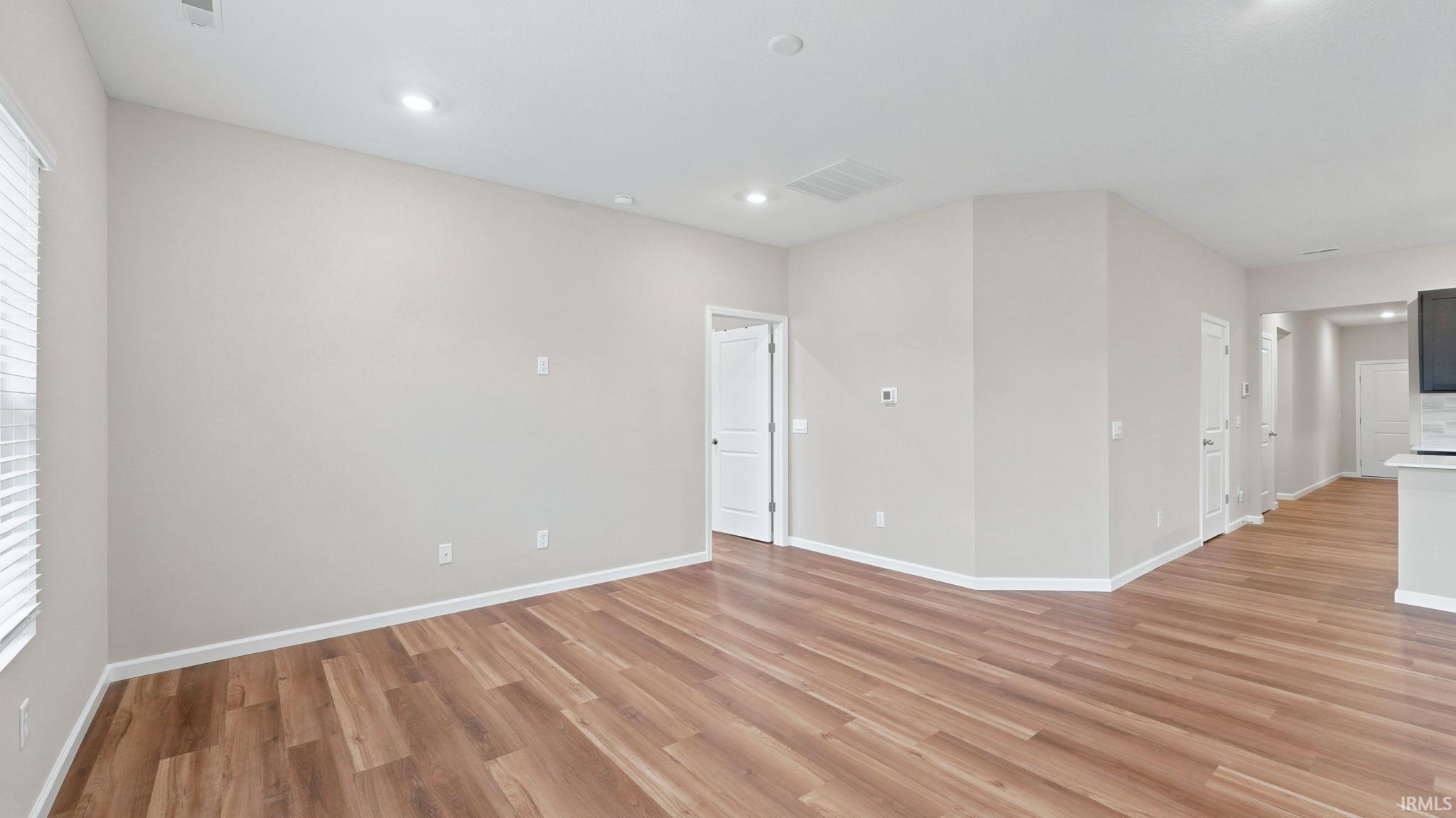 Spacious open-concept room featuring wood-finish flooring, light neutral wall paint, and recessed ceiling lighting