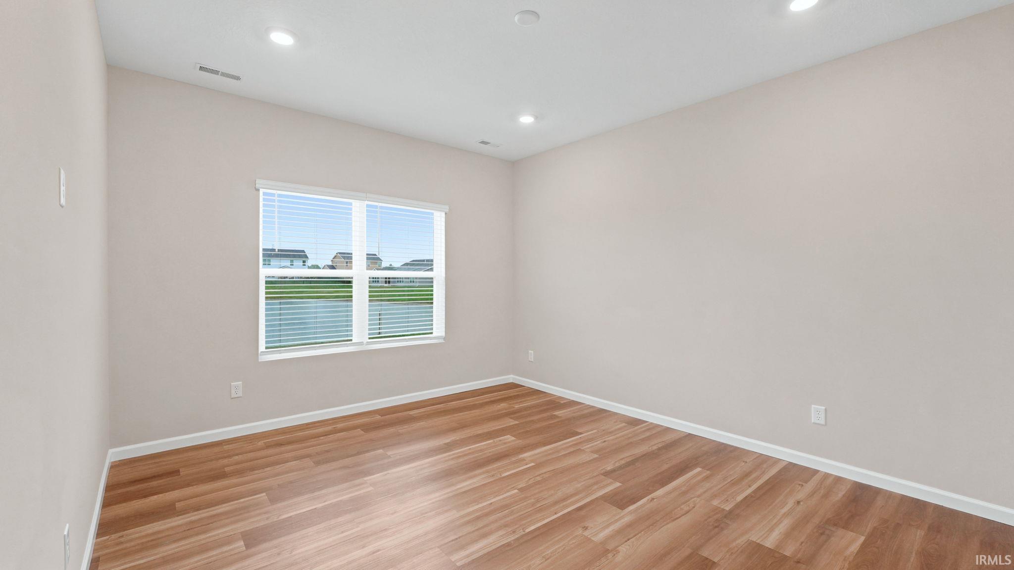Bright interior room featuring a large window with horizontal blinds, wood-finish flooring, recessed lighting, and light-toned walls