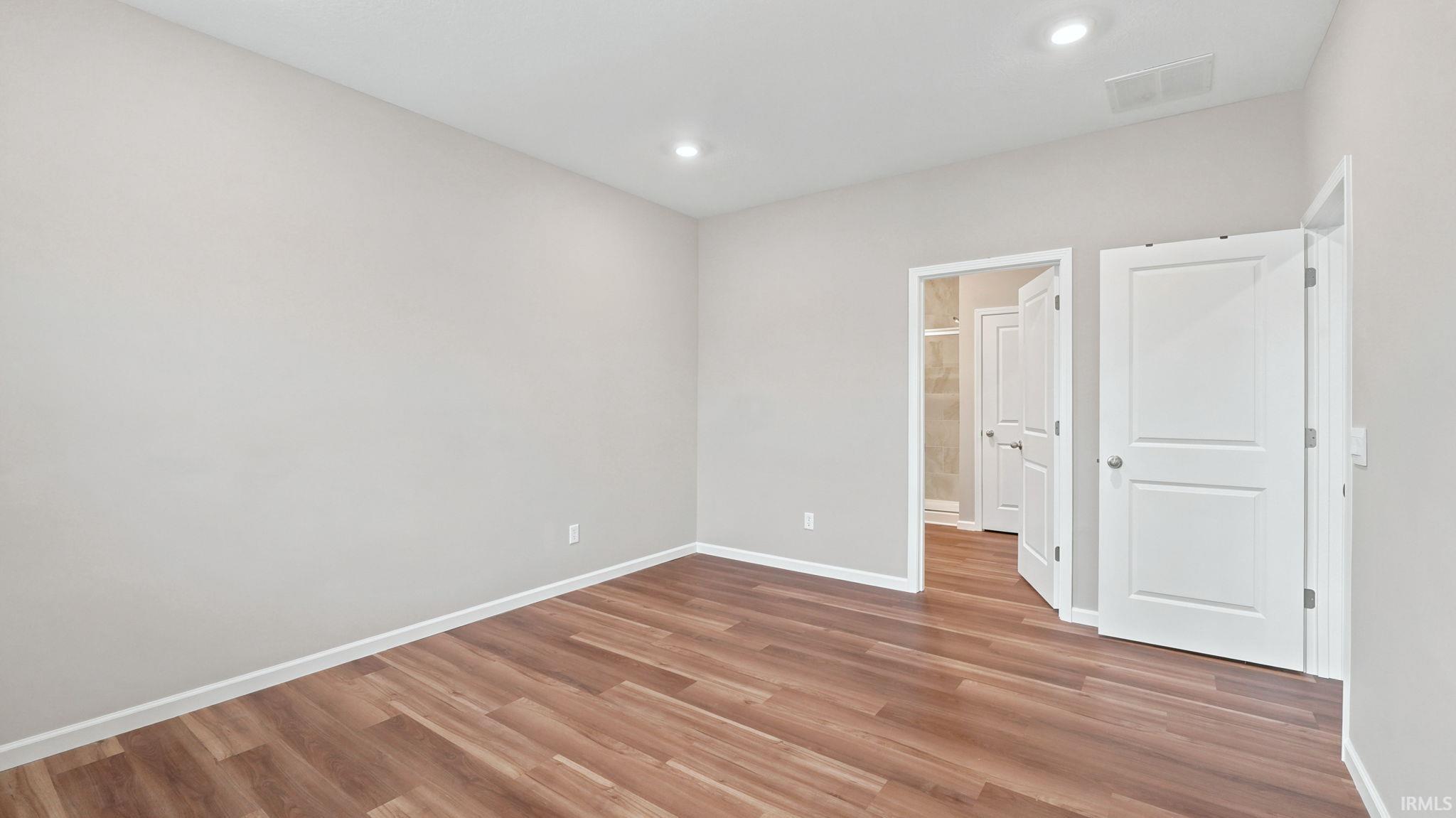 Spacious room featuring wood-finish flooring, light grey painted walls, white baseboards, and recessed lighting