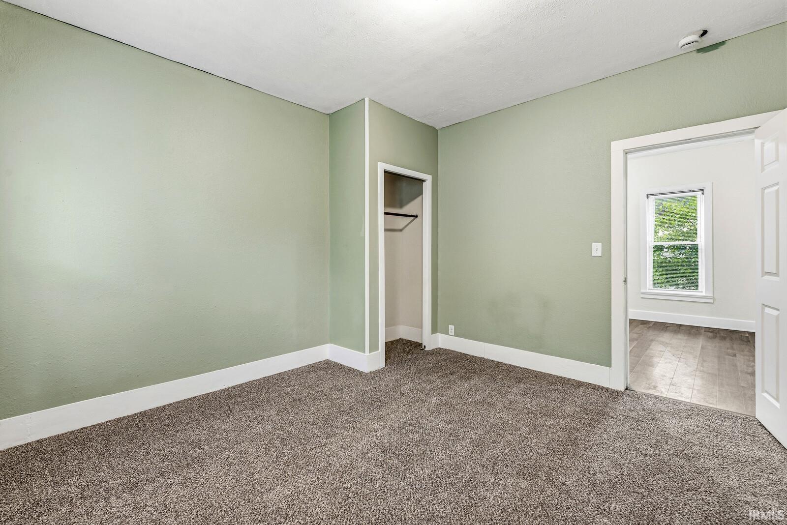 Carpeted interior room with light green walls, white trim, and a built-in closet with hanging rod