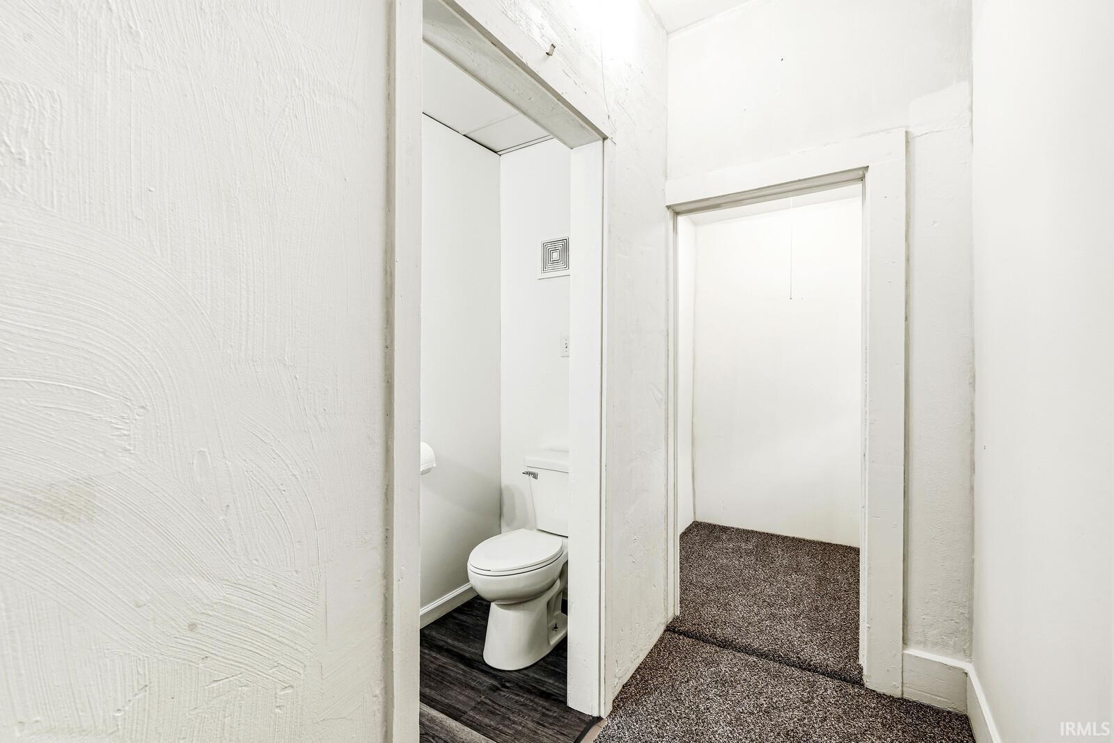Compact powder room featuring a toilet with a white tank and bowl, dark wood-finish flooring, and white walls