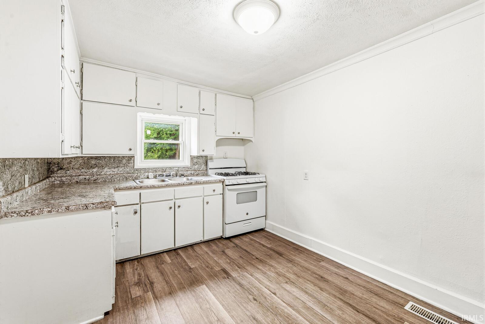 Compact kitchen featuring white cabinetry, a double basin sink, and a white gas range