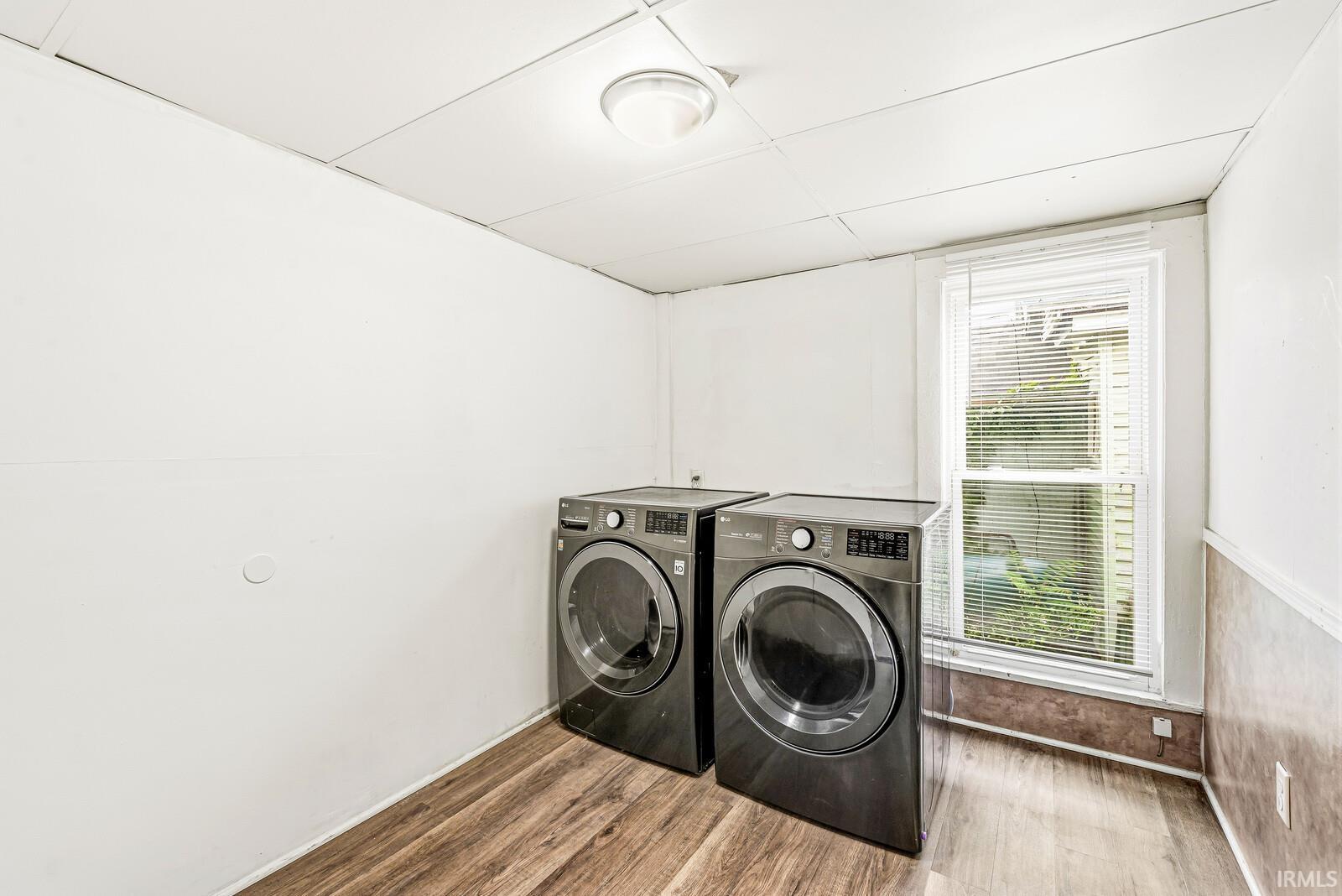 Dedicated laundry area featuring wood-finish flooring, white walls, and a single window with blinds