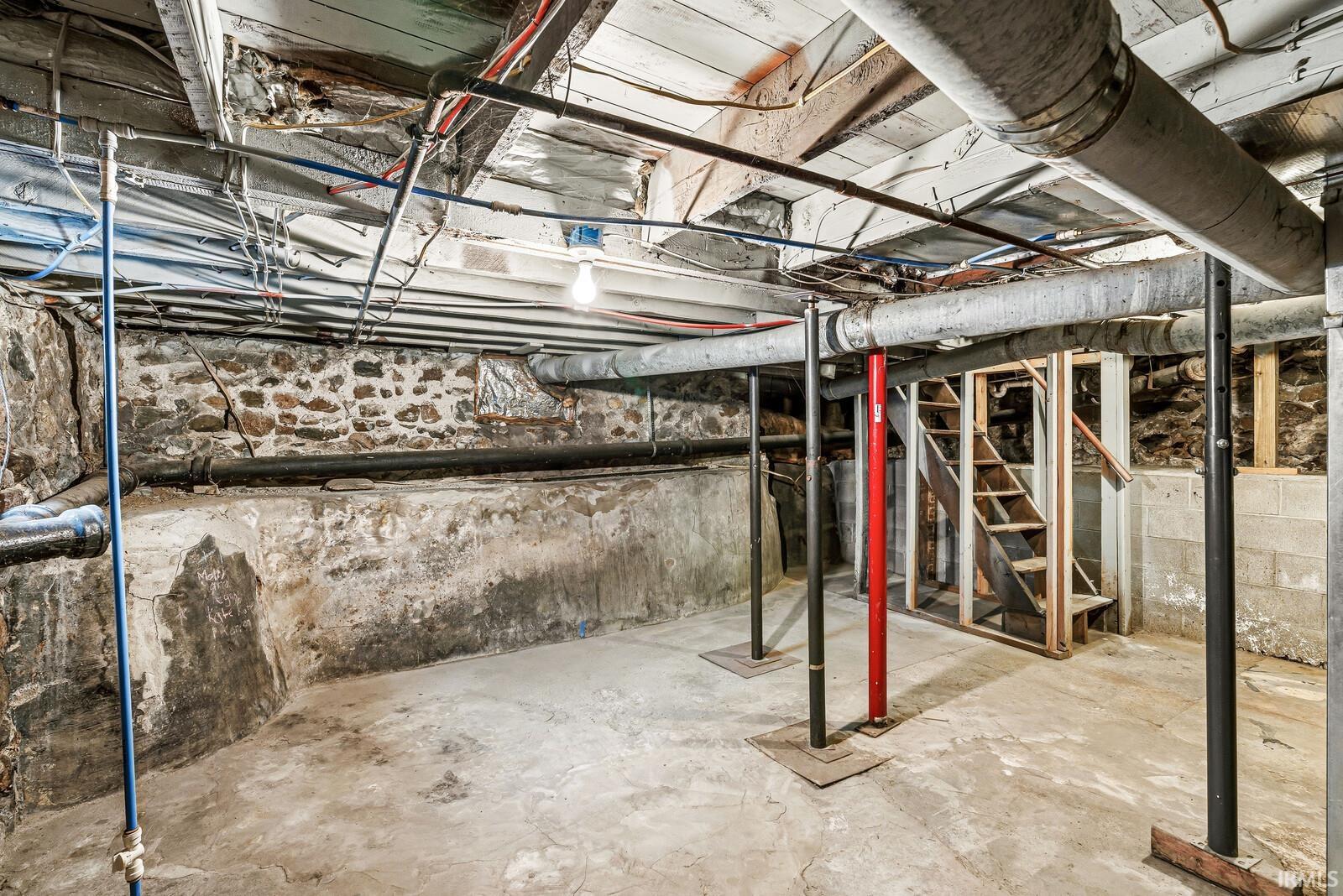 Unfinished basement space featuring exposed stone foundation walls, concrete flooring, and exposed utility lines