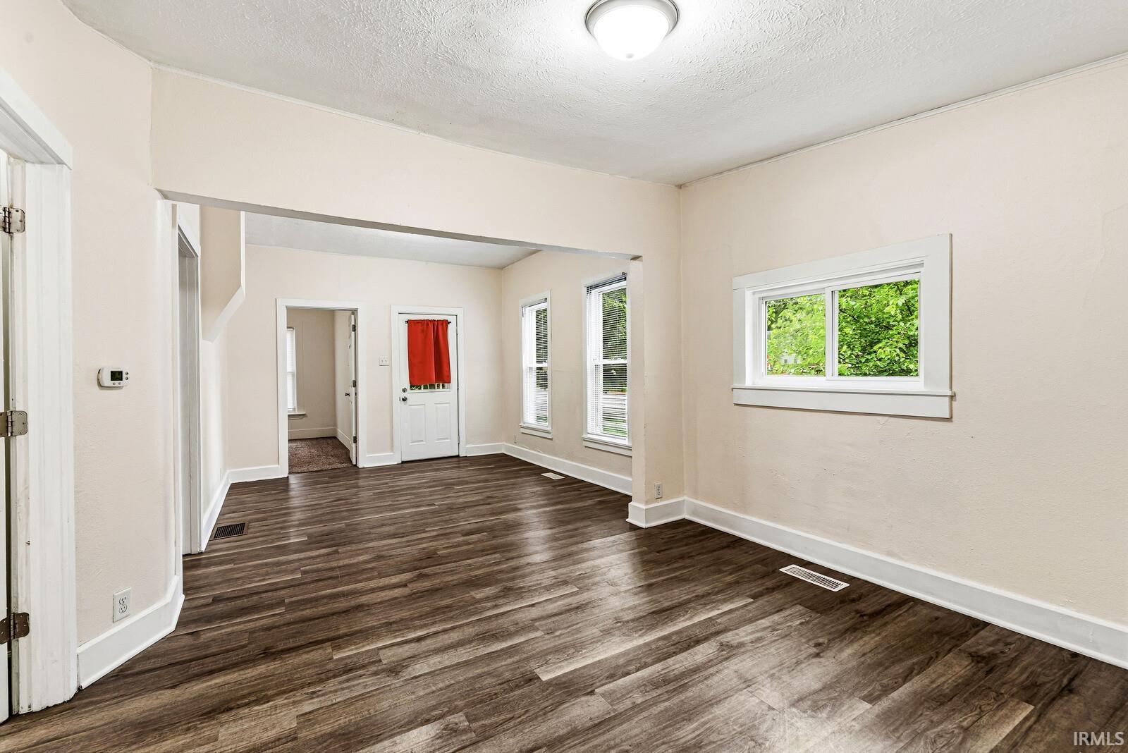 Spacious interior featuring wood-finish flooring, light neutral wall tones, white trim, and multiple windows