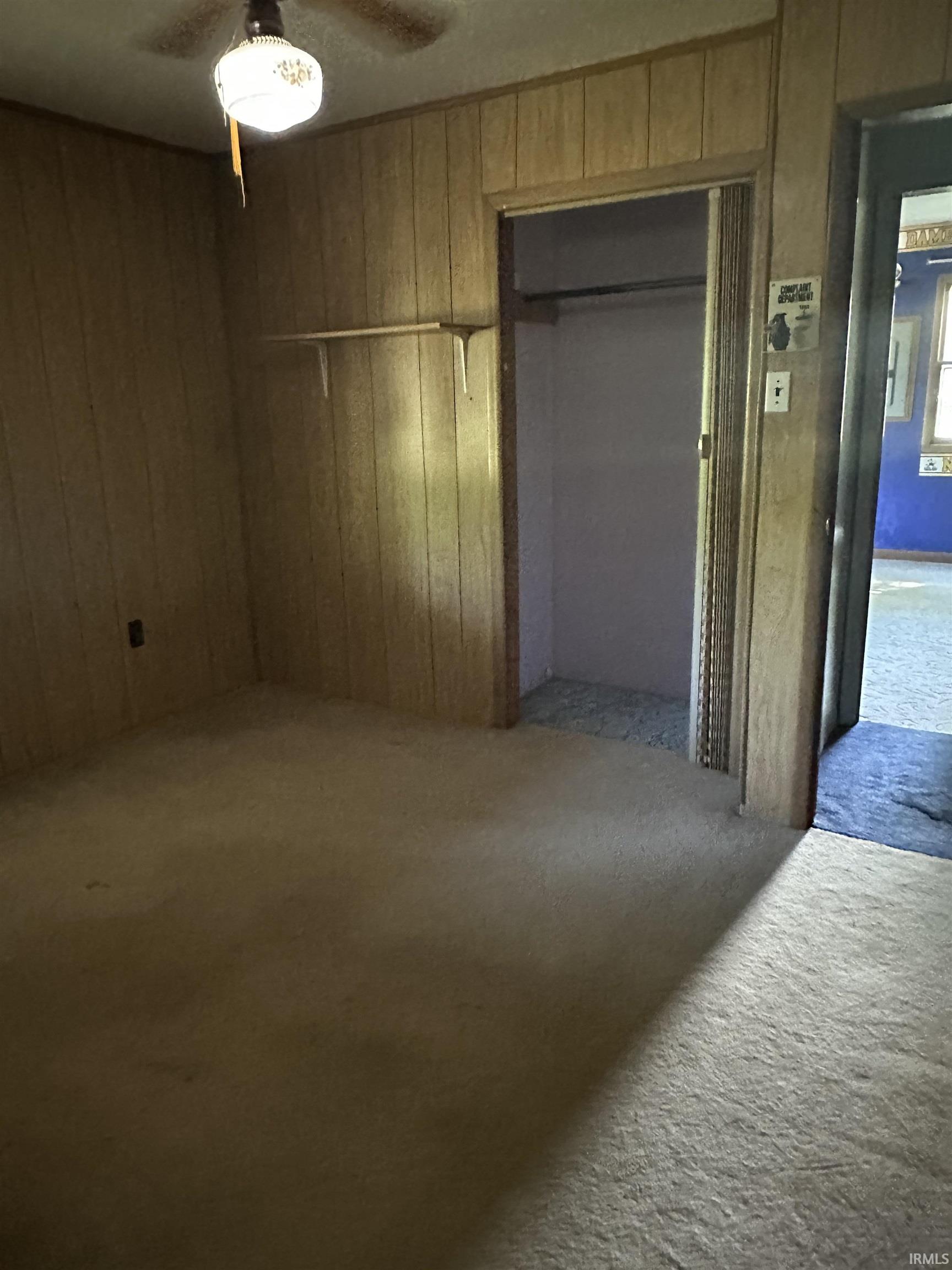 Room featuring wood-paneled walls, carpet flooring, a ceiling fan with integrated lighting, and a closet with bifold doors