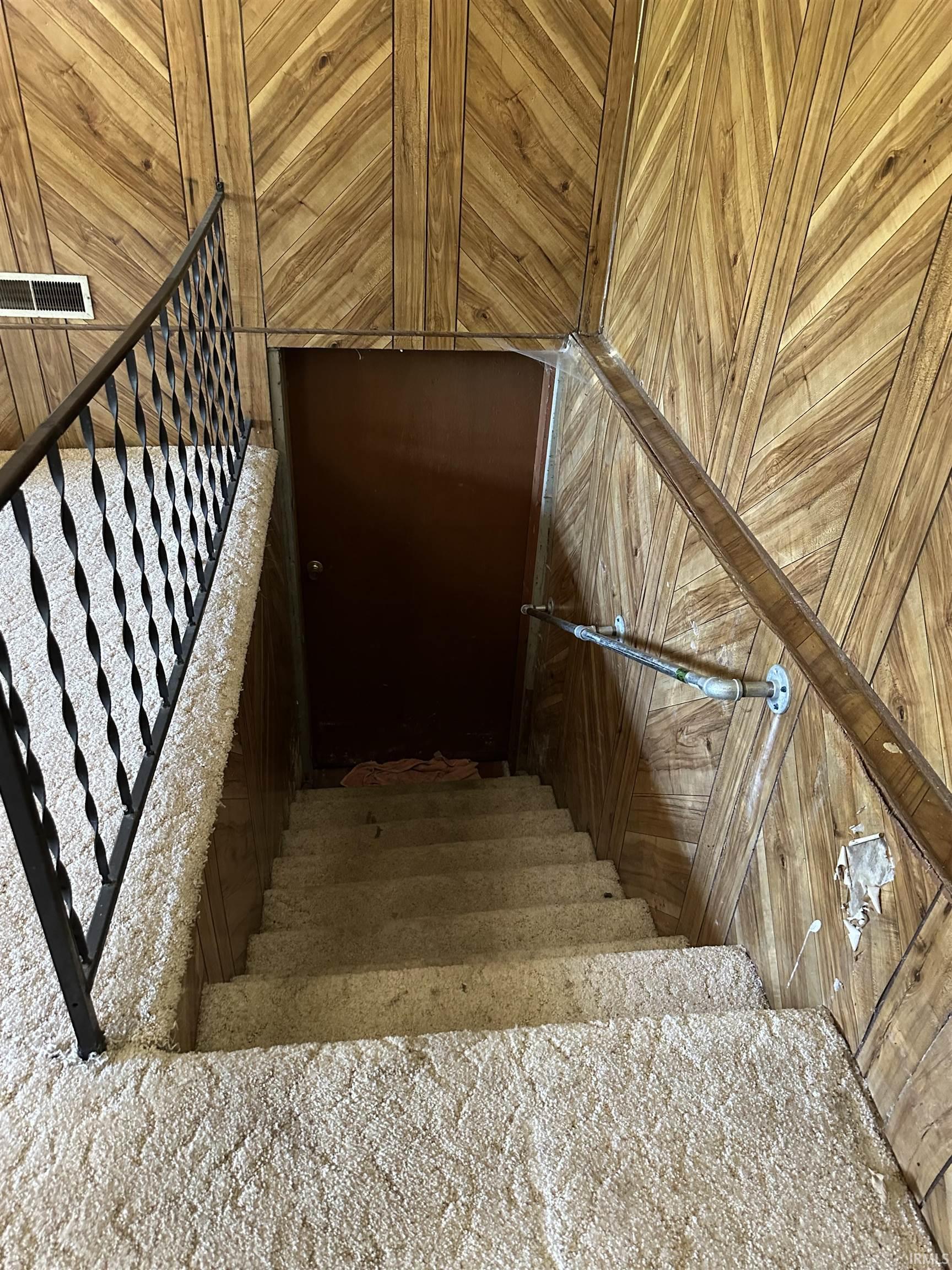 Staircase entry featuring wood paneling, wrought iron railing, and carpeted steps