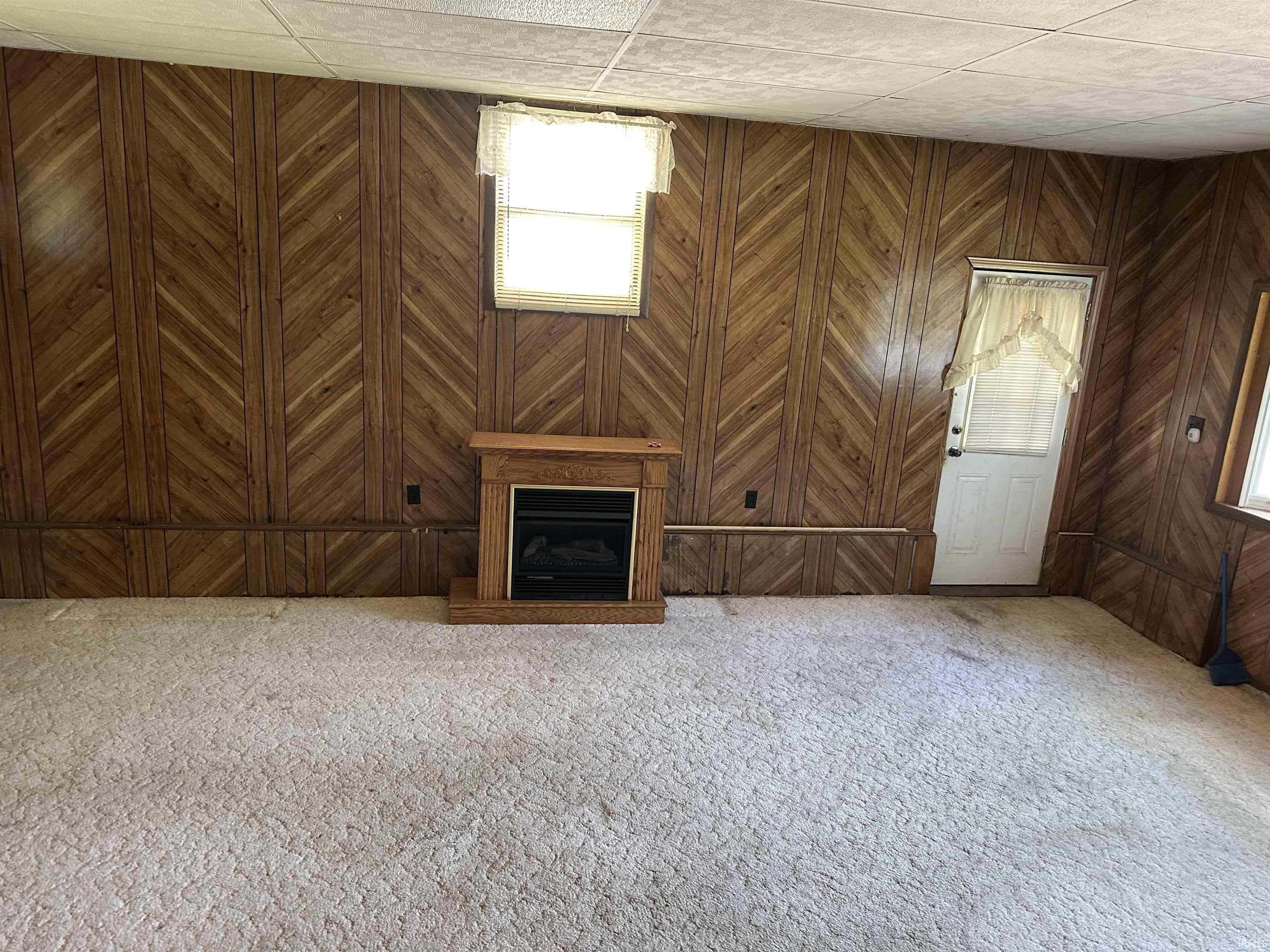 Room featuring chevron-patterned wood paneling, a built-in fireplace with wood-finish mantel, and light-colored carpet flooring