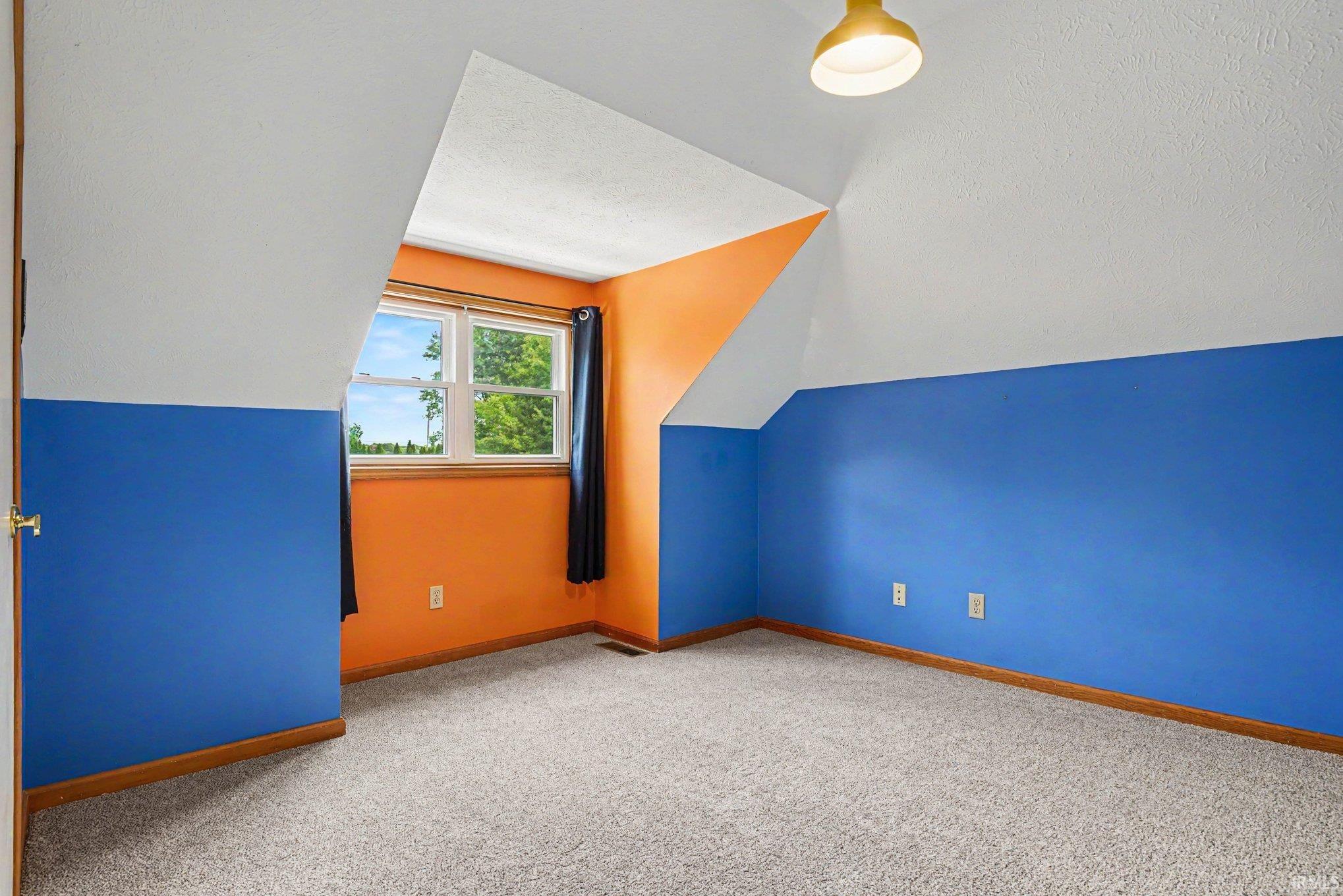 Room featuring sloped ceilings, a window with exterior visibility, and neutral carpet flooring