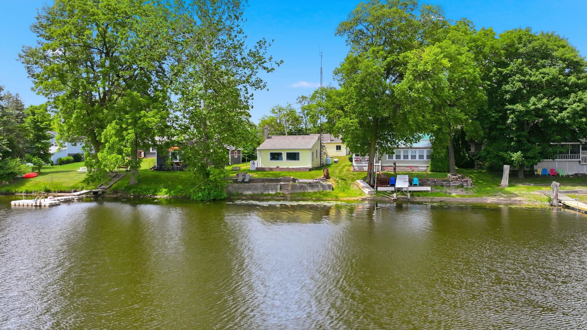 Waterfront property featuring a private floating dock, mature trees, a manicured lawn, and direct water access