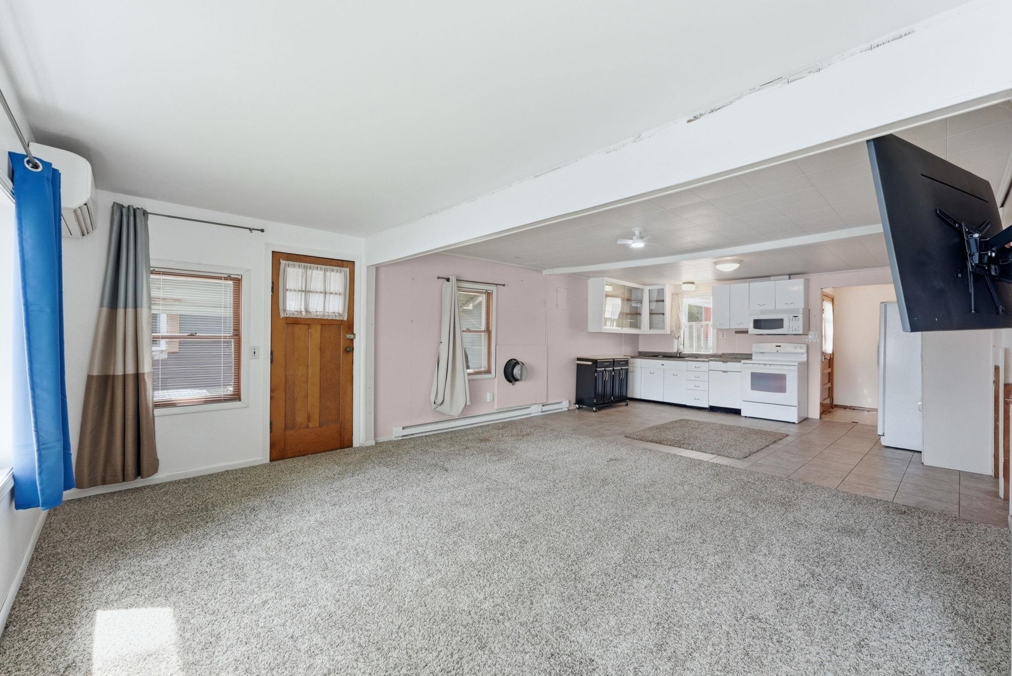 Open-concept living space with light-toned carpeting and a kitchen featuring white cabinetry and appliances