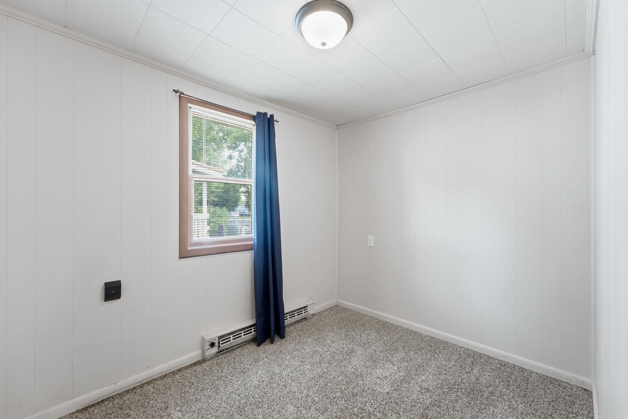 Room featuring light gray wall paneling, ceiling-mounted flush light fixture, and a window with wood-finish trim