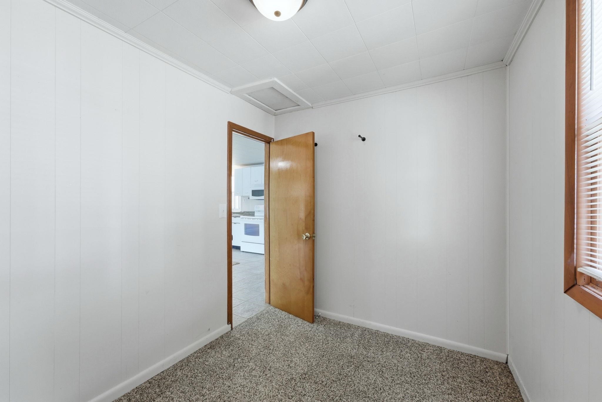 Carpeted room with white panel walls and a wood-frame window with horizontal blinds