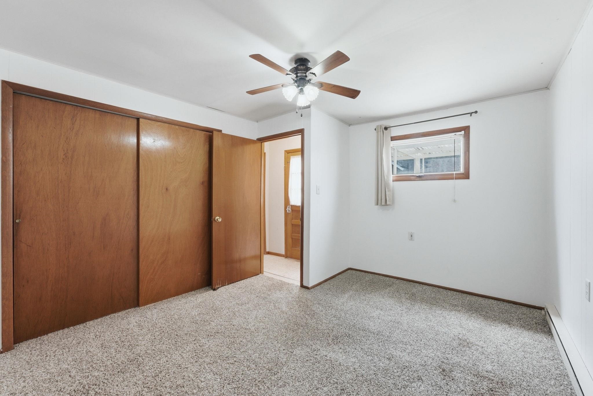 Carpeted room featuring a ceiling fan with light, wood-paneled closet doors, and a window with wood trim