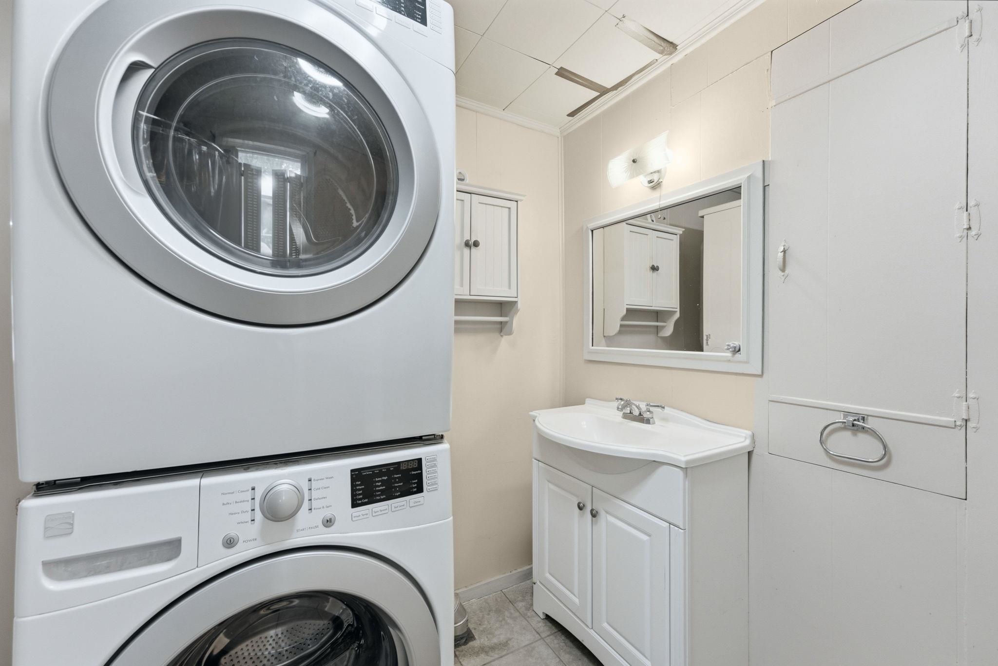 Dedicated laundry area featuring a stackable washer and dryer, adjacent to a vanity with a white cabinet and integrated sink