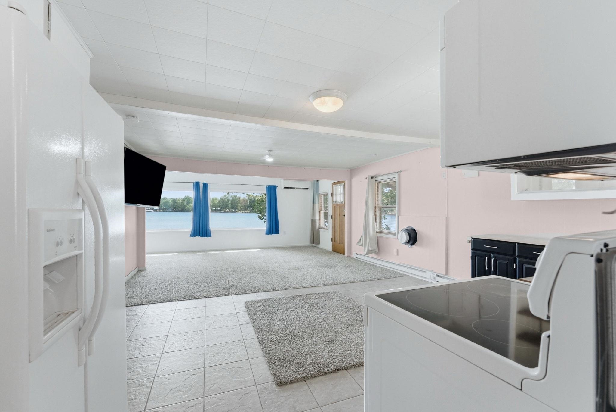 Open-concept kitchen and living area featuring tile flooring, carpeted living space, and exposed ceiling beams