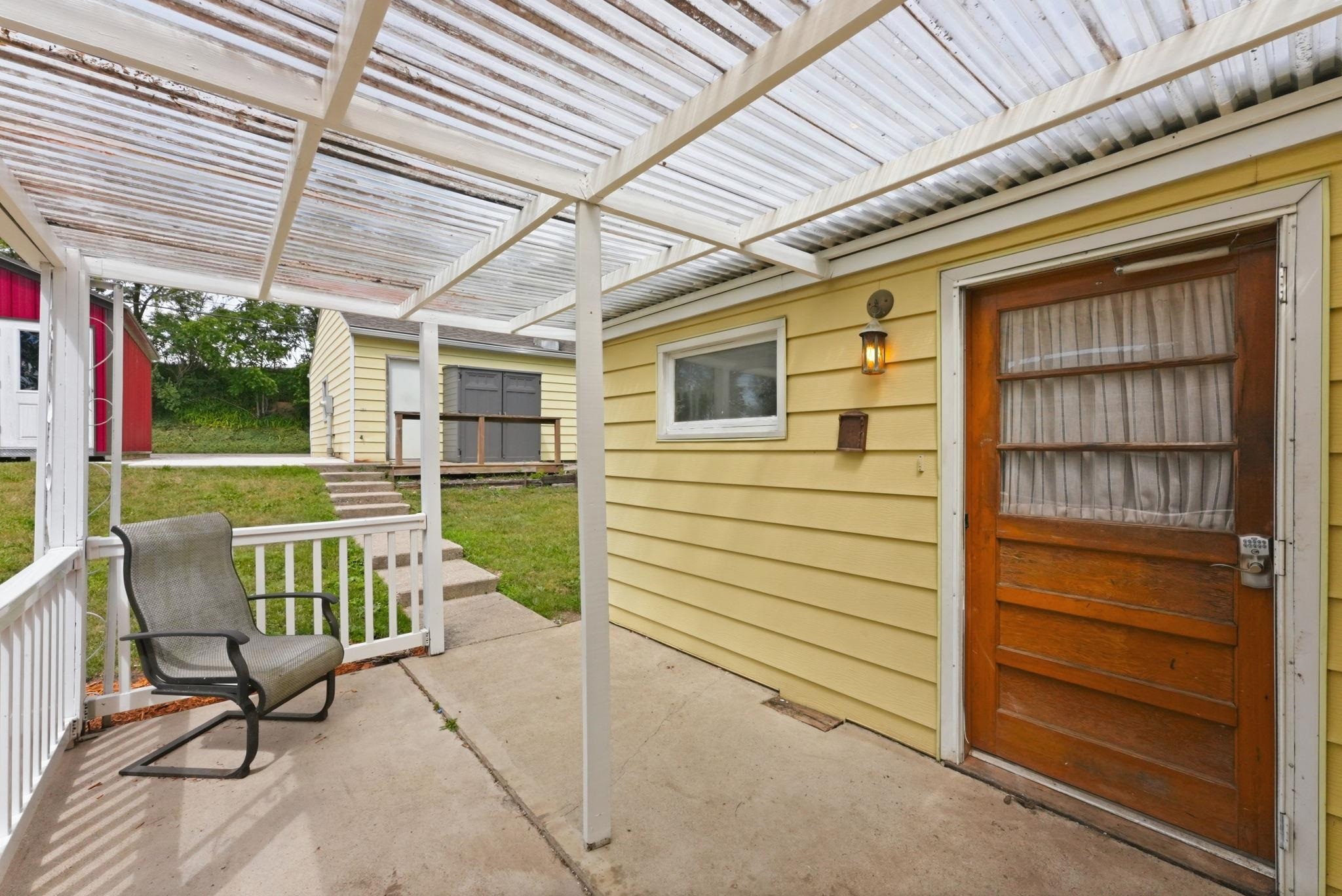 Covered patio with concrete flooring, white railing, and a corrugated translucent roof