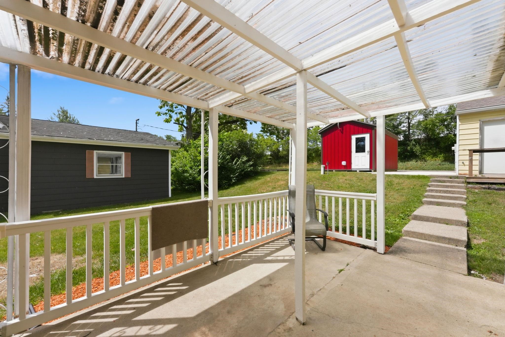 Covered concrete patio featuring a white railing and a corrugated translucent roof