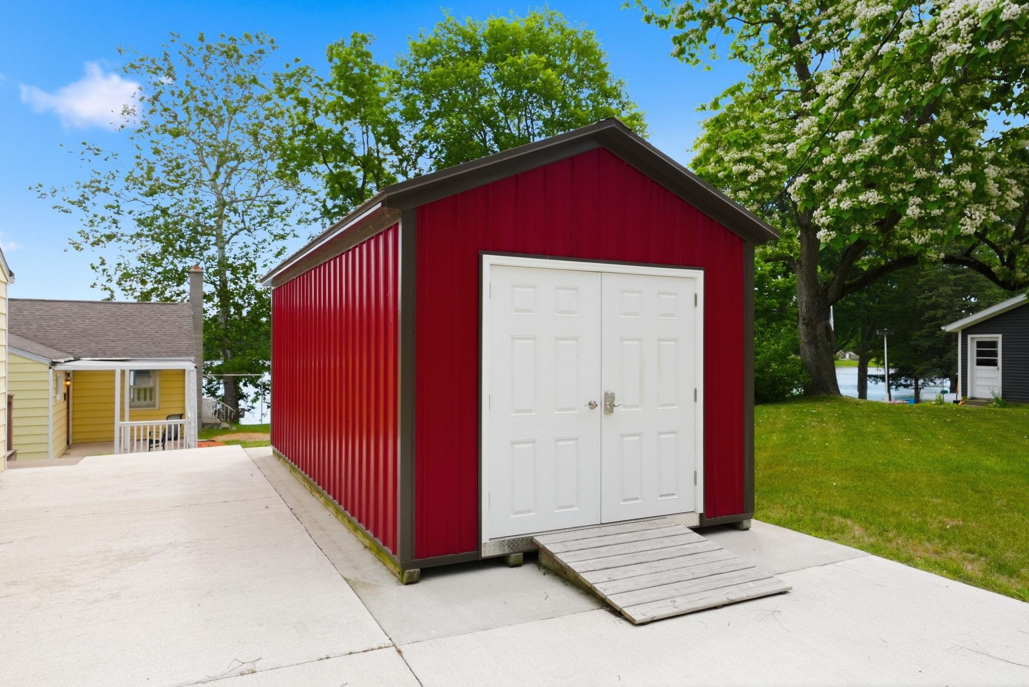 Red metal shed featuring white double doors and a wood ramp